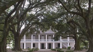 Still from film that shows large white house under canopy of trees