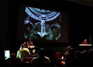 an audience watching a black and white film of a man in a bowler hat